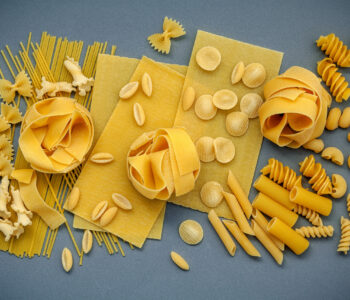 Italian foods concept and menu design. Assorted types of pasta Farfalle, Pasta A Riso, Orecchiette Pugliesi, Gnocco Sardo and Farfalle  setup on gray background with flat lay.